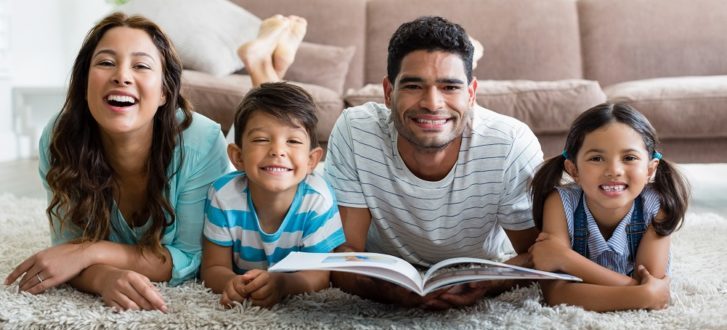 Portrait of parents and children lying on rug and reading book