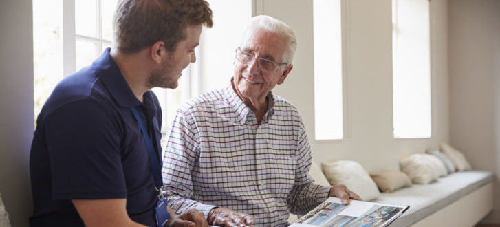 Senior man sitting looking at photo album with male nurse
